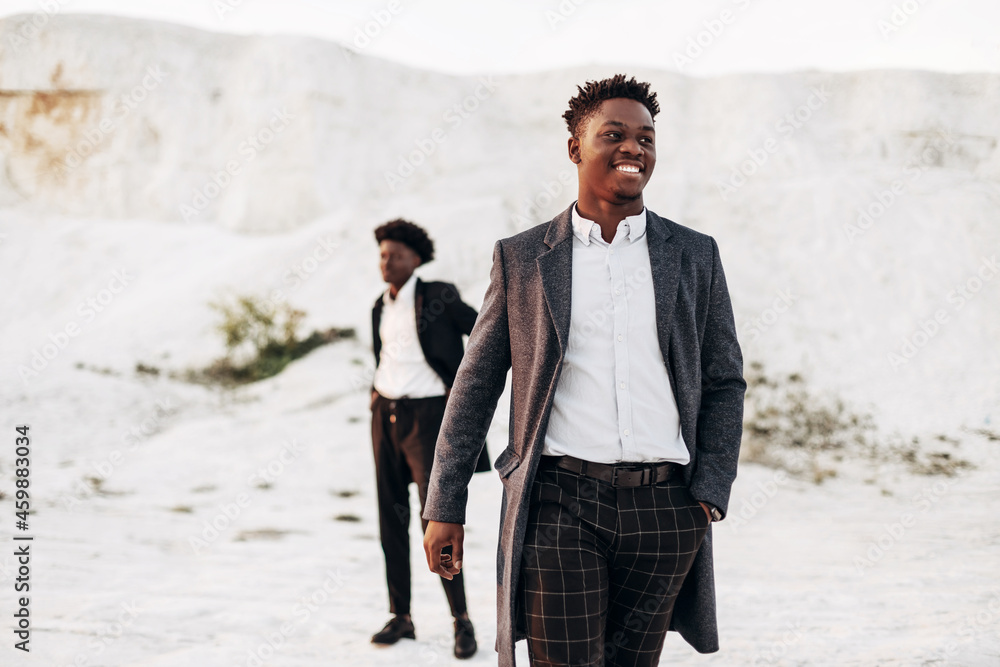 Fashion portrait of two handsome male models, in suits, on the street against the background of rocky mountains Fashion portrait of two handsome male models, in suits, on the street against the background of rocky mountains