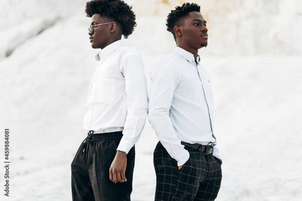 Two trendy American men posing back to back against the backdrop of white mountains Two trendy American men posing back to back against the backdrop of white mountains