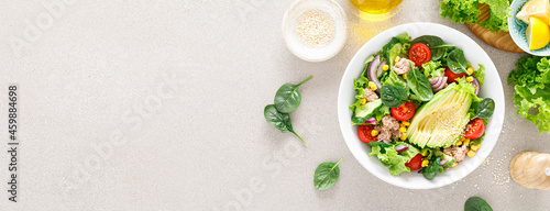 Avocado and tuna fresh vegetable salad with tomato, cucumber corn, onion, lettuce and spinach. Healthy and detox food concept. Ketogenic diet. Buddha bowl dish on light background, top view