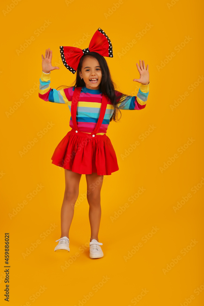 a dark-skinned happy girl in a red skirt in a colored jacket with a red polka dot bow on her head on a yellow background a dark-skinned happy girl in a red skirt in a colored jacket with a red polka dot bow on her head on a yellow background