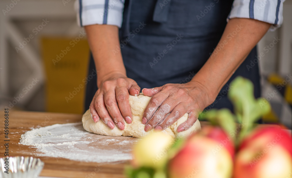 Cook hands kneading dough, piece of dough with white wheat flour. Low key shot, close up on hands, some ingredients around on table.