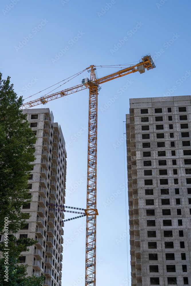 Construction crane and unfinished monolithic concrete frame of residential buildings under construction against clear blue sky