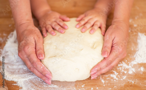Mother and child hands prepares the dough with flour on rustic wooden table from above. Homemade pastry for bread or pizza. Bakery background.