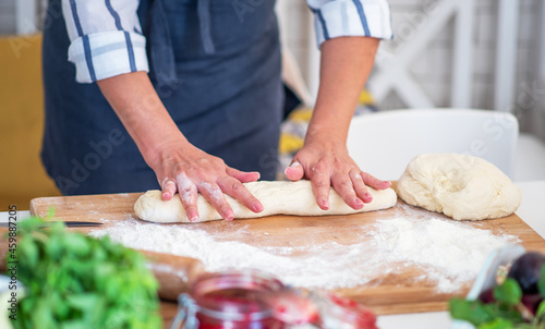 Female hands making dough. Dough with flour, eggs and other utensil, ingredients lies on white wooden table. Baking homemade process.