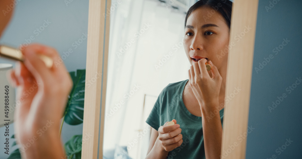Beautiful Asia lady with casual cloth put lipstick on her lips in front of mirror in bedroom at home in morning before go dating outside. Smiling young woman applying makeup and looking at mirror. Beautiful Asia lady with casual cloth put lipstick on her lips in front of mirror in bedroom at home in morning before go dating outside. Smiling young woman applying makeup and looking at mirror.