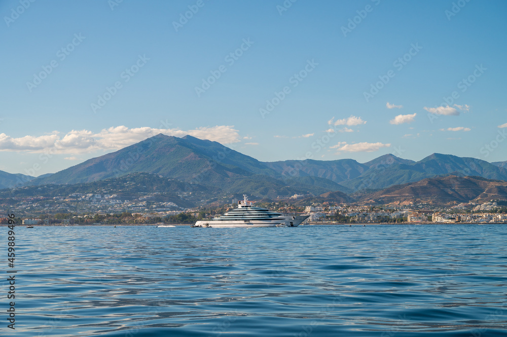 starboard side of a luxury mega yacht of more than 100 meters docked outside of puerto banus. landscape with the mountains of marbella