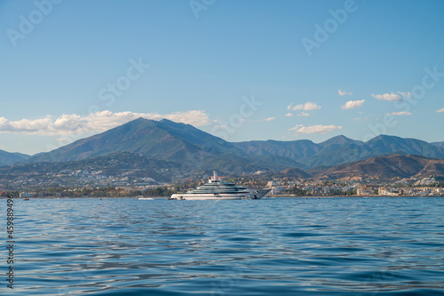 starboard side of a luxury mega yacht of more than 100 meters docked outside of puerto banus. landscape with the mountains of marbella