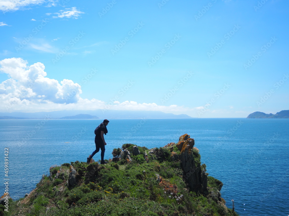 a man on a cliff over some wild rocks with the ocean and the white clouds in the background 