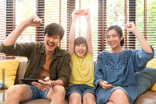 family quality time,asian parent and son sit relax playing game console or smart together laugh joyful smiling on sofa couch in living room at home,asian family homs isolation quarantine ideas concept