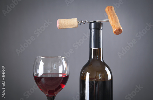 Bottle of red wine with glass and corkscrew.