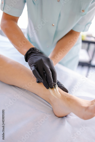 Legs depilation with sugar paste. Close-up of lifestyle ankle hair removal process in the salon. Hands in black latex gloves. Shugaring procedure professional service. sugaring