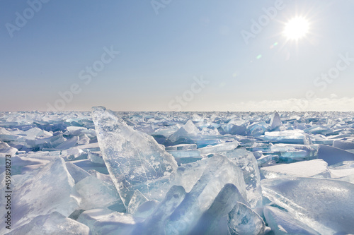 The sun over the endless ice hummock field on a frosty winter day. Piles of snow-covered fragments of blue transparent ice. Cool natural background. Unusual winter landscape of frozen Baikal Lake