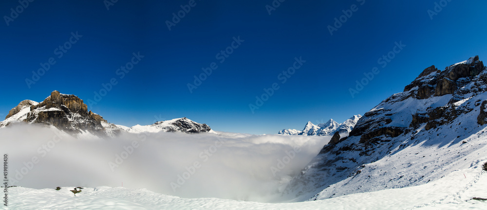 Panorama of snow-covered swiss alps with sea of fog and blue sky 
