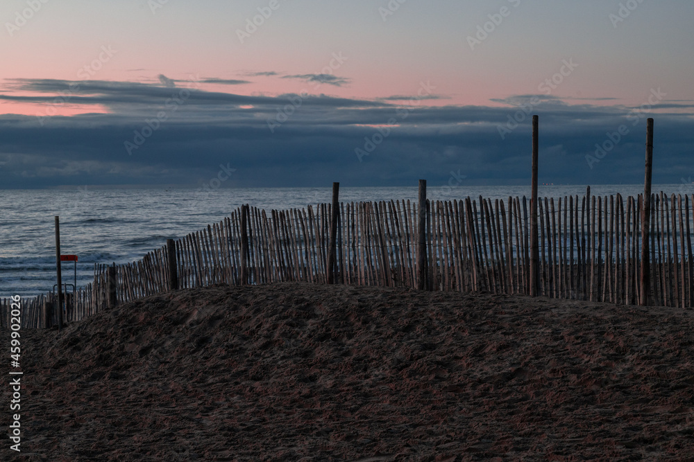 Fence of wooden posts at dusk on the beach of Zandvoort, Netherlands.
