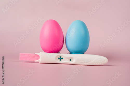A positive pregnancy test on a pink background and pink and blue eggs, determining the gender of the unborn child