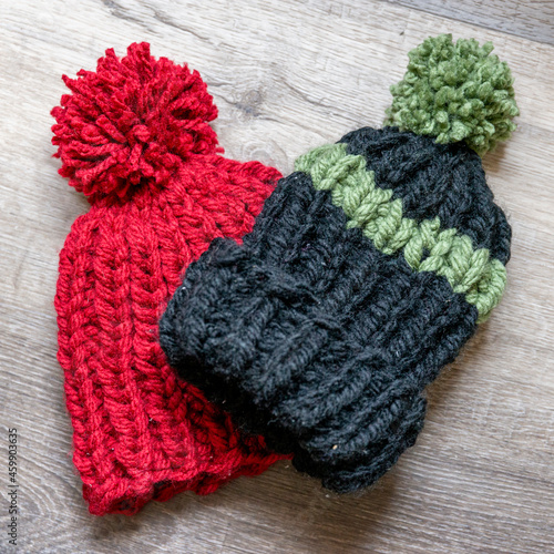 Hand knit winter hats, just completed and ready to be used.  Children's size with pom pom on top.  Bright red and stripped knit hats on grey wood background.  Flat lay with window light.
