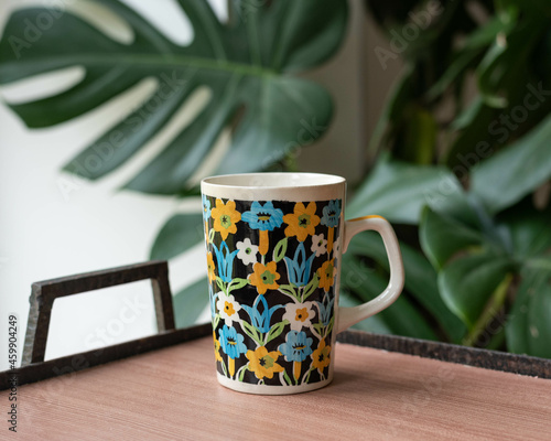 Mid-century modern porcelain cup on a wooden table with plants in the background