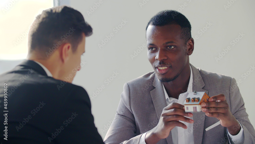 Real-estate black agent showing house model to client in office Real-estate black agent showing house model to client in office