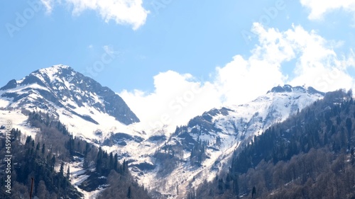 picturesque landscape of snow-capped mountains with white clouds on a blue sky on a sunny day at Krasnaya Polyana in Sochi, Russia