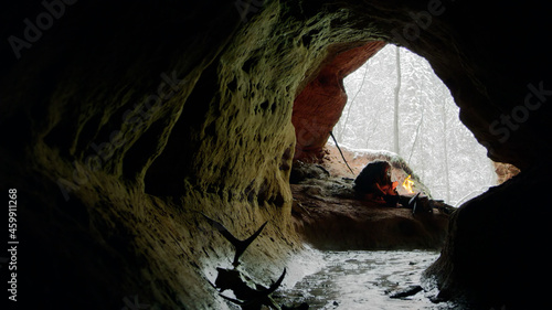 Wild caveman sitting near bonfire in dark cave photo