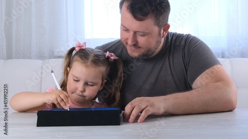 cute little girl 3 years old and her father draw draws on the tablet and at home watching a drawing lesson online. Dad rejoices at his daughters success and helps her in her studies. Online school