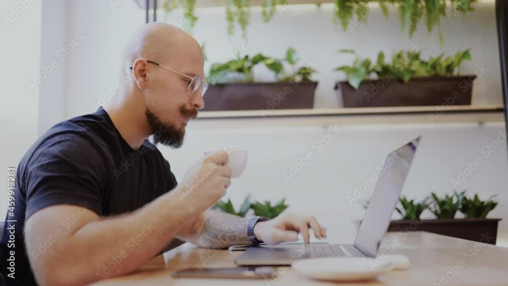Millennial Caucasian man with mustache and beard freelancer businessman diligently works on laptop in cafe drinks coffee Millennial Caucasian man with mustache and beard freelancer businessman diligently works on laptop in cafe drinks coffee