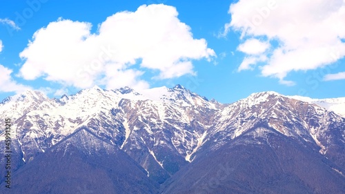 beautiful landscape of snow-capped mountains with white clouds on blue sky on a sunny day at Krasnaya Polyana in Sochi, Russia. Famous ski resort