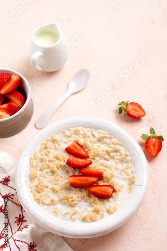 Oatmeal porridge with strawberries in a white plate on a linen napkin on pink background. Breakfast health food concept. Top view