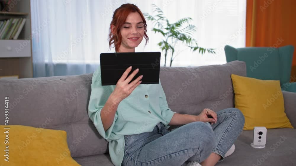 portrait girl checking the video feed on gadget, young happy woman studying the work of security camera using tablet pc while sitting on couch at home portrait girl checking the video feed on gadget, young happy woman studying the work of security camera using tablet pc while sitting on couch at home