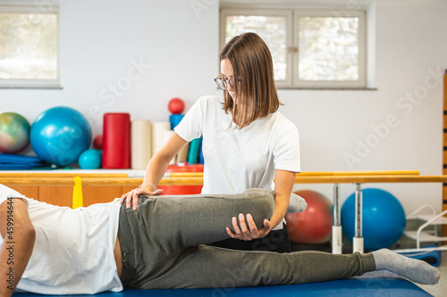 Female physiotherapist doing leg and hip stretching treatment on a male patient Fotobehang