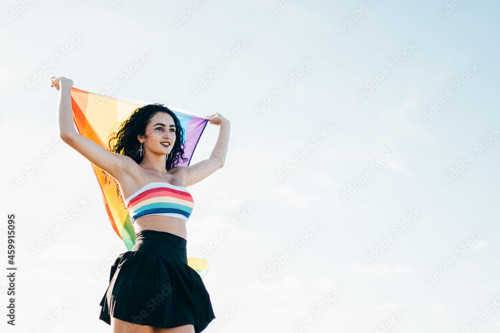 Young woman holding a lgbt flag from behind. Dressed in a colorful top Young woman holding a lgbt flag from behind. Dressed in a colorful top