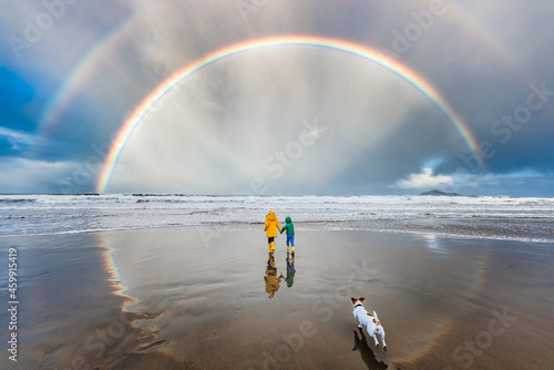 Dog running after children under double rainbow at beach photo