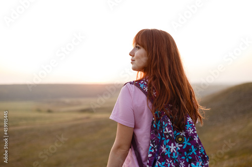 Young redhead woman with backpack looks away in sunset photo