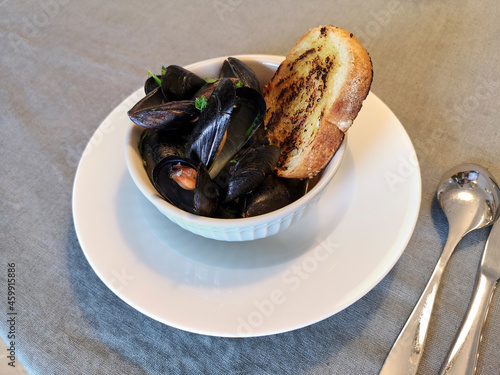 Bowl filled with boiled mussels and a slice of toasted bread.