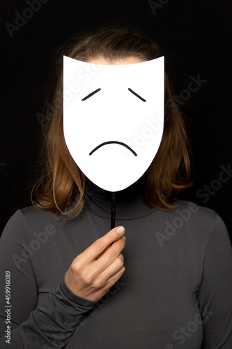 A woman is holding a mask with a sad emotion. Unhappy face.