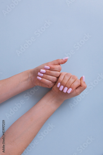 Beautiful women's hands with a pink manicure on a blue background. Top view. Clean skin.