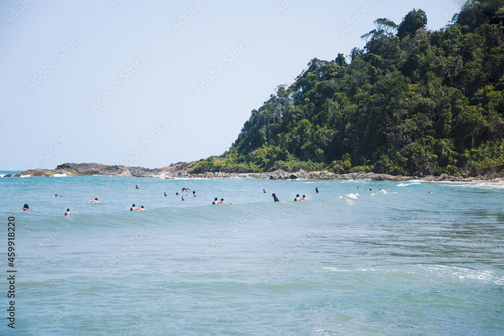 Travelers swimming in wavy ocean against mount with trees Travelers swimming in wavy ocean against mount with trees