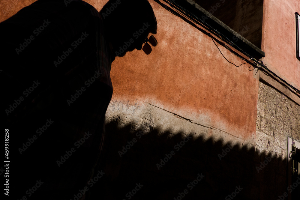 Fototapeta premium Makarska, Croatia People in silhouette walk along a red wall with a shadow of a roof projected.