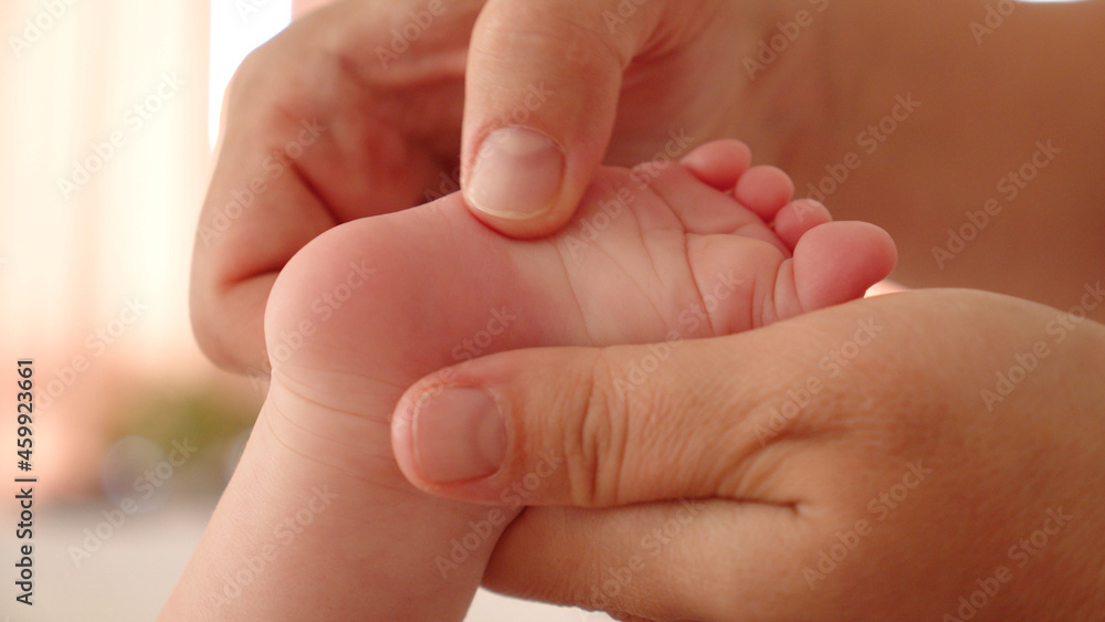 Mother doing massage for her healthy infant baby. Small caucasian newborn laying on his belly while his mother is performing a massage for his small feet and developing toes. . Mother doing massage for her healthy infant baby. Small caucasian newborn laying on his belly while his mother is performing a massage for his small feet and developing toes. .
