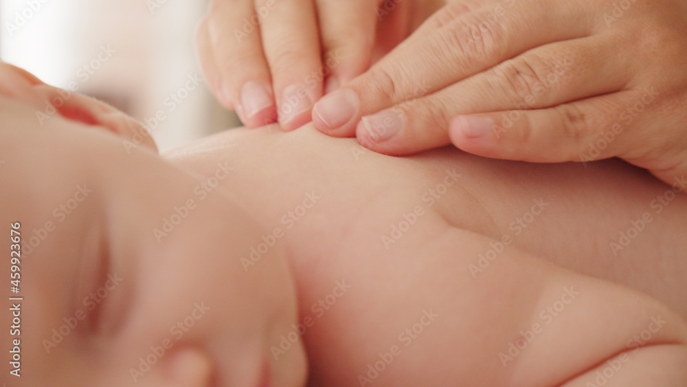 Mother doing massage on her healthy sleeping infant baby. Small caucasian newborn resting and laying on his belly while his mother is performing a massage for his small back and developing muscles. . Mother doing massage on her healthy sleeping infant baby. Small caucasian newborn resting and laying on his belly while his mother is performing a massage for his small back and developing muscles. .