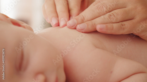 Mother doing massage on her healthy sleeping infant baby. Small caucasian newborn resting and laying on his belly while his mother is performing a massage for his small back and developing muscles. . © Valua Vitaly