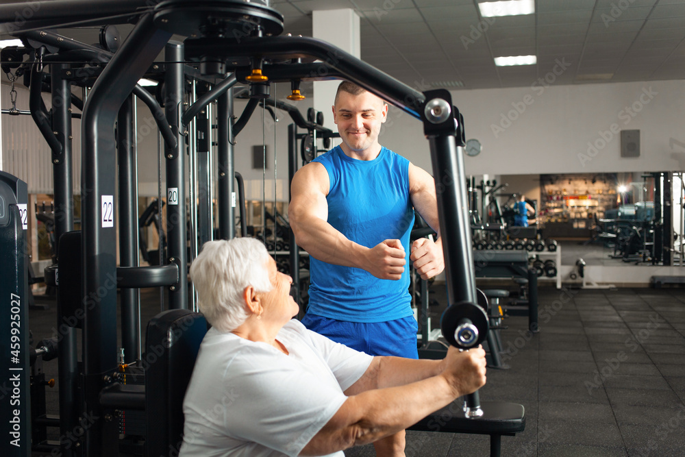 Portrait of person on a simulator in a gym. senior concept, a woman and a coach lead a healthy lifestyle, engage in physical education, stretching. Rehabilitation after injuries, happy Portrait of person on a simulator in a gym. senior concept, a woman and a coach lead a healthy lifestyle, engage in physical education, stretching. Rehabilitation after injuries, happy