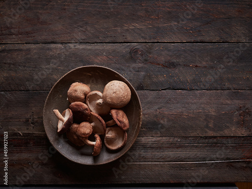 fresh whole shiitake mushrooms, lentinula edoes, on a dark plate on a dark wooden table, top view with copy space photo