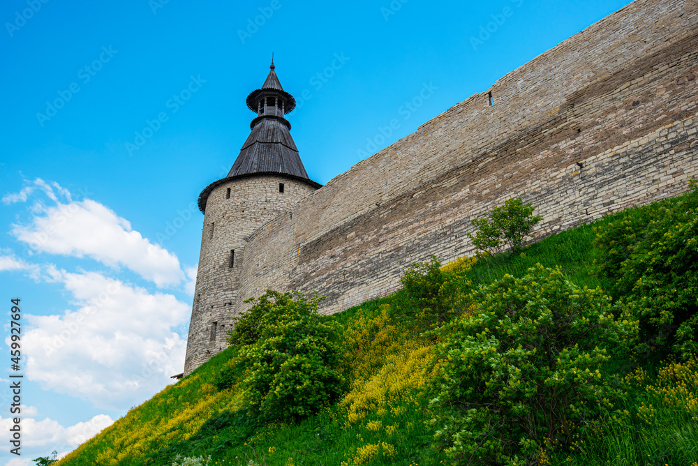 The fortress wall of a medieval fortification with towers against a bright blue sky.