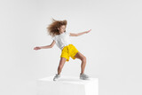 Full-length portrait of smiling girl in casual clothes standing on big box isolated on white studio background. Happy childhood concept.