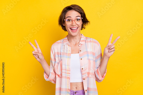 Photo of cheerful excited nice young woman show hands v-signs smile good mood isolated on yellow color background
