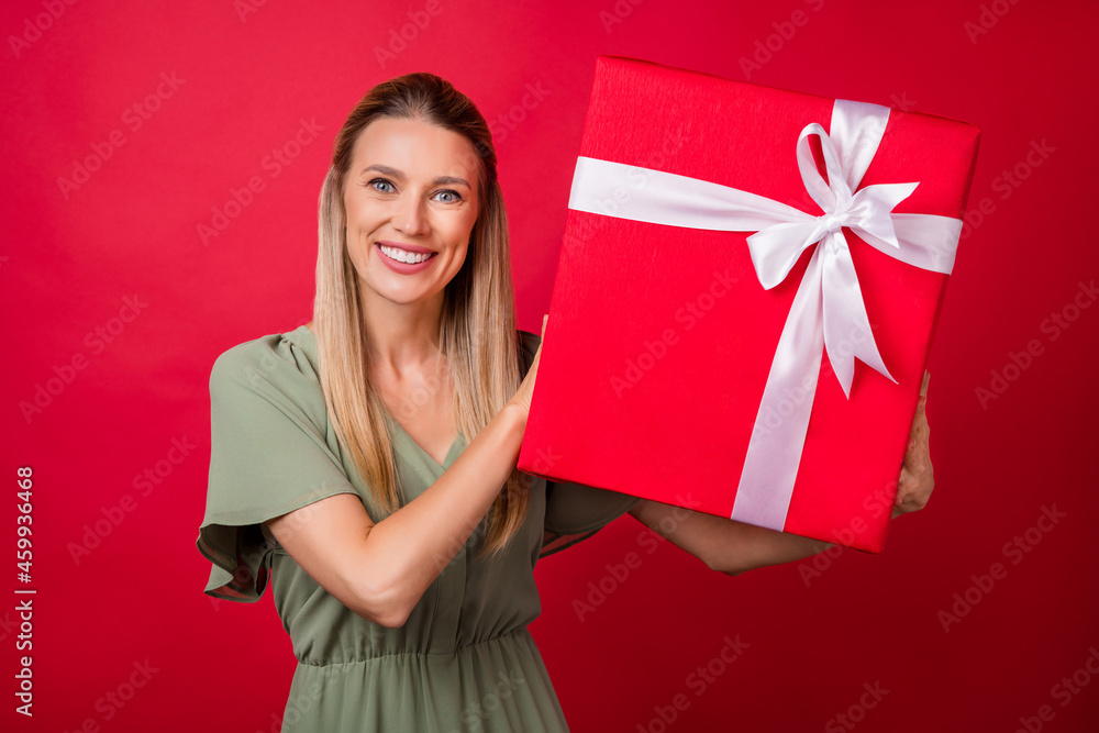 Photo of impressed young blond lady hold box wear khaki dress isolated on red color background Photo of impressed young blond lady hold box wear khaki dress isolated on red color background