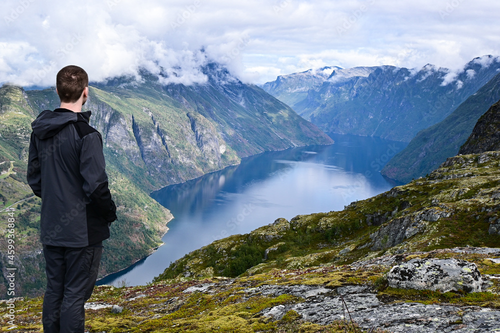 Man looking at amazing aerial views of a typical norwegian Fjord from a mountain.