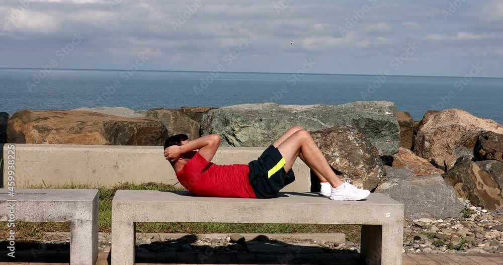 Strong sporty athletic fit man 2wear sports clothes warm up training doing abdominal abs exercises over sea beach outdoor on concrete pier seaside in summer day. Strong sporty athletic fit man 2wear sports clothes warm up training doing abdominal abs exercises over sea beach outdoor on concrete pier seaside in summer day.
