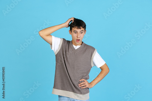 Portrait of young man, student or boy in casual clothes isolated on blue studio backgroud. Human emotions concept. photo